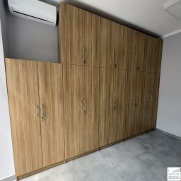I WOOD DESIGN - Duża, jasna szafa z drewnianymi frontami, zamykana na klucz, sięgająca sufitu, z widocznym klimatyzatorem na ścianie. Nowoczesny design.