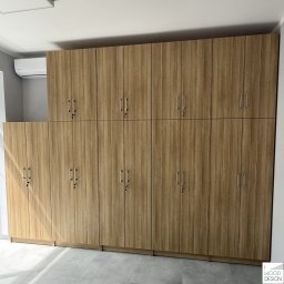 I WOOD DESIGN - Długa, drewniana szafa zamykana na klucz, z widocznymi srebrnymi uchwytami, zajmująca całą ścianę, z klimatyzatorem na górze. Jasne wnętrze.