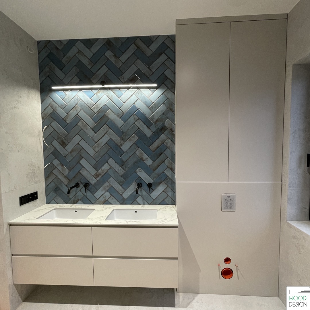 Nowoczesna łazienka z szafką na wymiar, dwoma umywalkami na blacie marmurkowym i niebieską ścianą w jodełkę. Uwagę zwraca minimalistyczny design i oświetlenie LED.