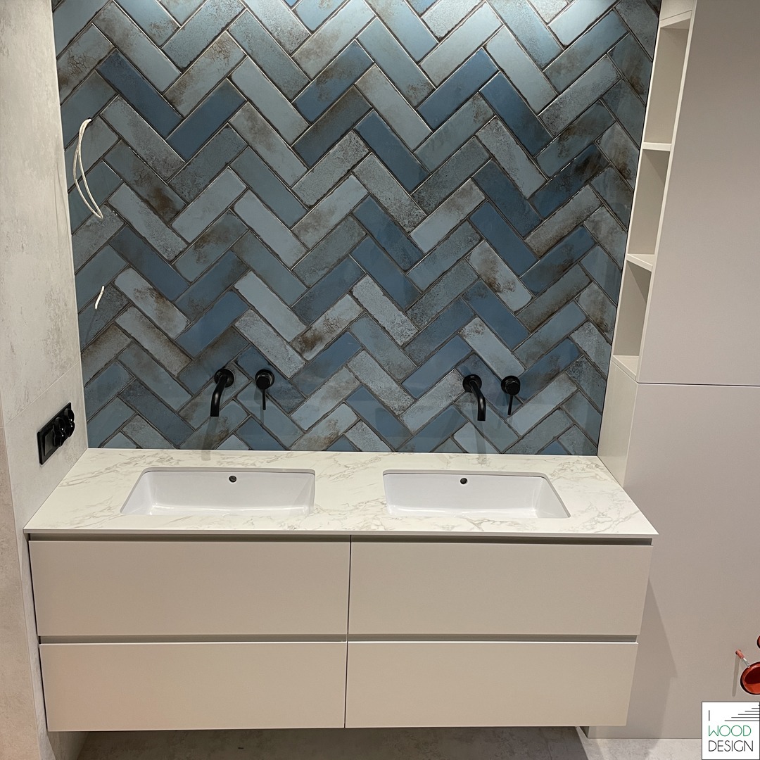 Łazienka z dwoma umywalkami na blacie z efektem marmuru, białe szafki pod umywalkami i ściana w niebieską jodełkę. Czarne baterie.