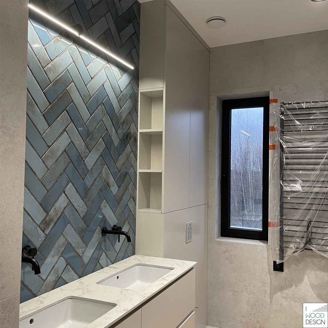 Nowoczesna łazienka z szafką na wymiar, umywalkami nablatowymi i niebieską ścianą w jodełkę, oświetloną listwą LED. Grzejnik drabinkowy w folii ochronnej.