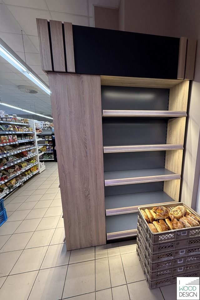 Regał sklepowy z płyty meblowej w supermarkecie w Białymstoku. Półki szare, góra czarna z elementami drewnianymi. W koszyku pieczywo.