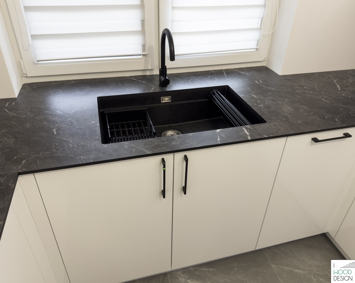 Czarny, granitowy blat kuchenny z wbudowanym, czarnym zlewem i minimalistycznymi, białymi szafkami. Nowoczesny design, widok z góry, oświetlenie naturalne.