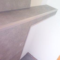 AIG-Company - Wykończenie schodów płytkami ceramicznymi w odcieniach szarości z aluminiowymi listwami krawędziowymi, widoczny fragment ściany z przygotowanym otworem na gniazdko elektryczne, podłoga...