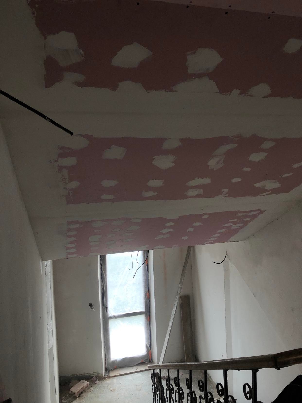 Klatka schodowa w trakcie prac wykończeniowych: sufit z widocznymi łatami po szpachlowaniu, przygotowany do dalszej obróbki, okno zakryte folią ochronną.