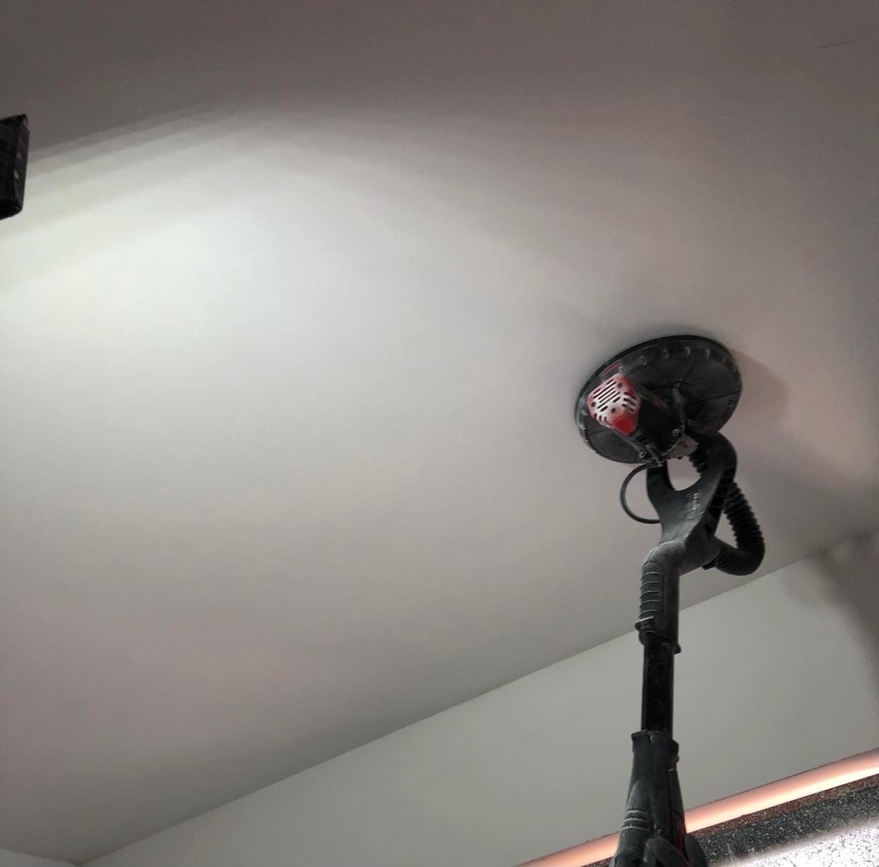 Szlifierka teleskopowa do gładzi na suficie, widoczne ślady szlifowania i fragment okna w tle.