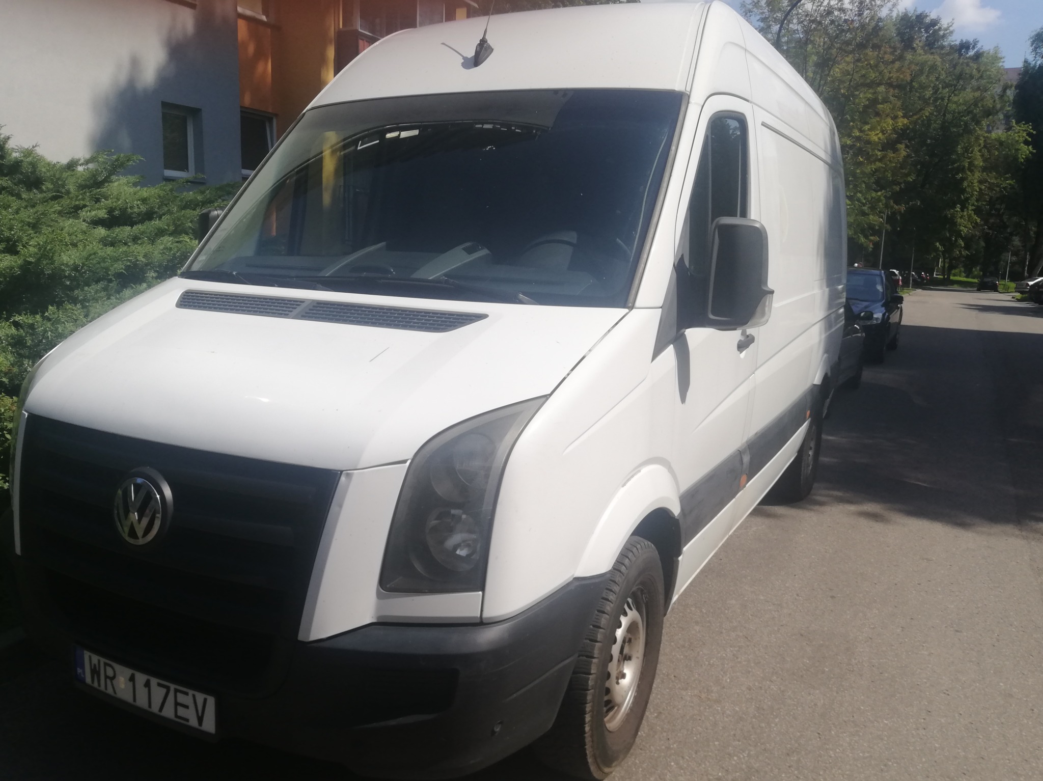 Biały samochód dostawczy Volkswagen Crafter zaparkowany na ulicy, widok z przodu z lekkim kątem, widoczna tablica rejestracyjna WR 117EV.