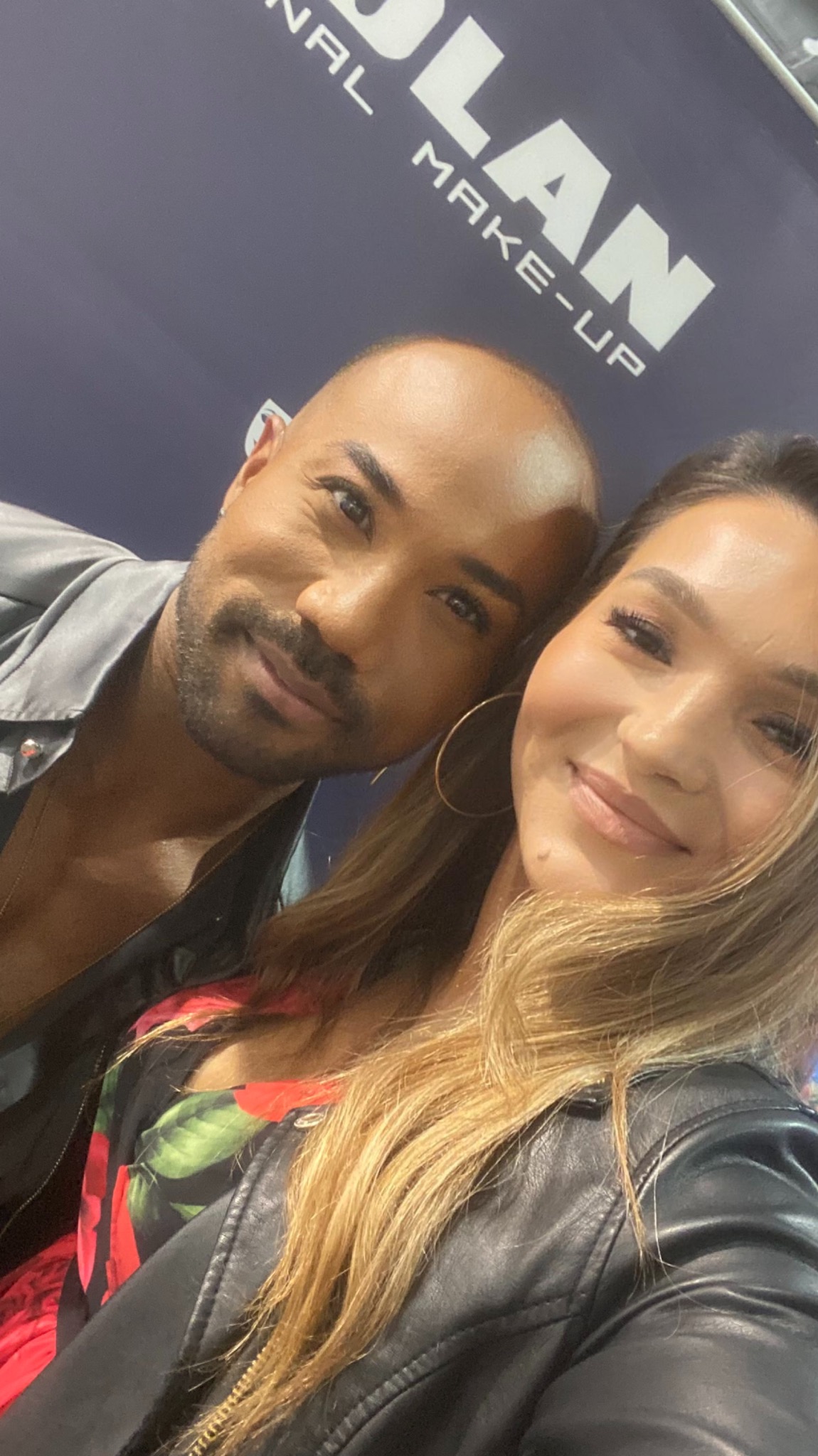 Selfie kobiety z blond włosami i mężczyzny z lekkim zarostem na tle logo firmy kosmetycznej