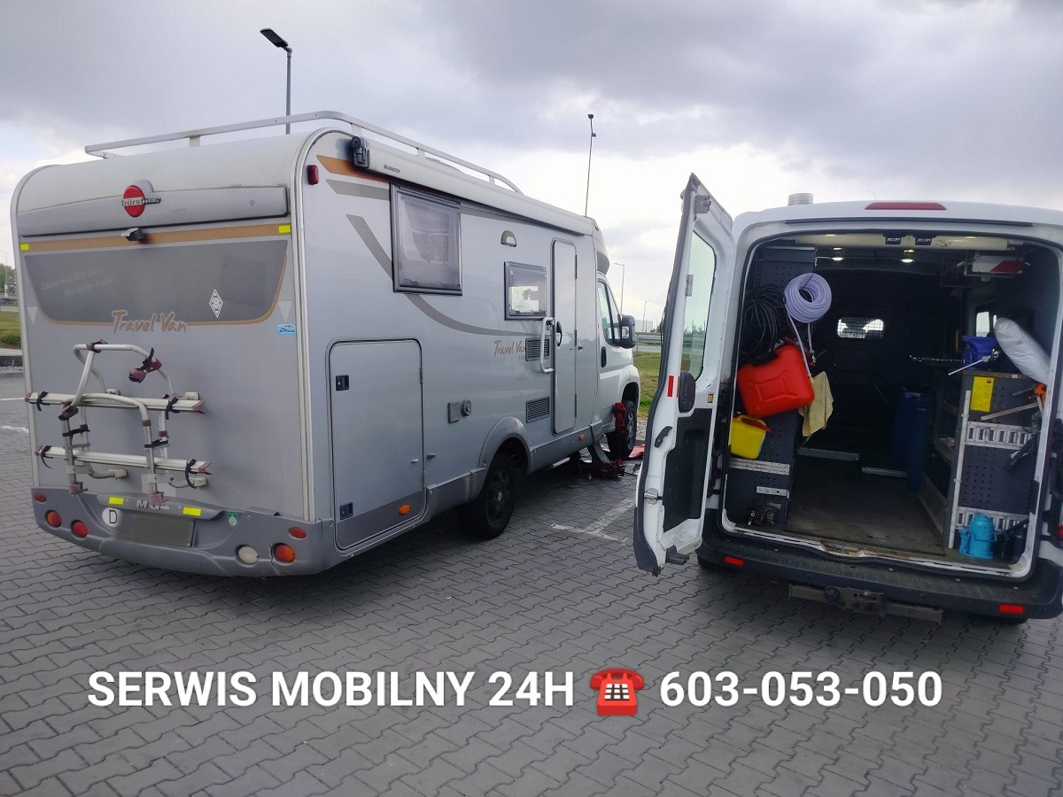 Awaria kampera 'Travel Van' na parkingu, podniesionego na lewarku, z otwartymi drzwiami busa serwisowego, w którym widoczne narzędzia i kanister z paliwem.