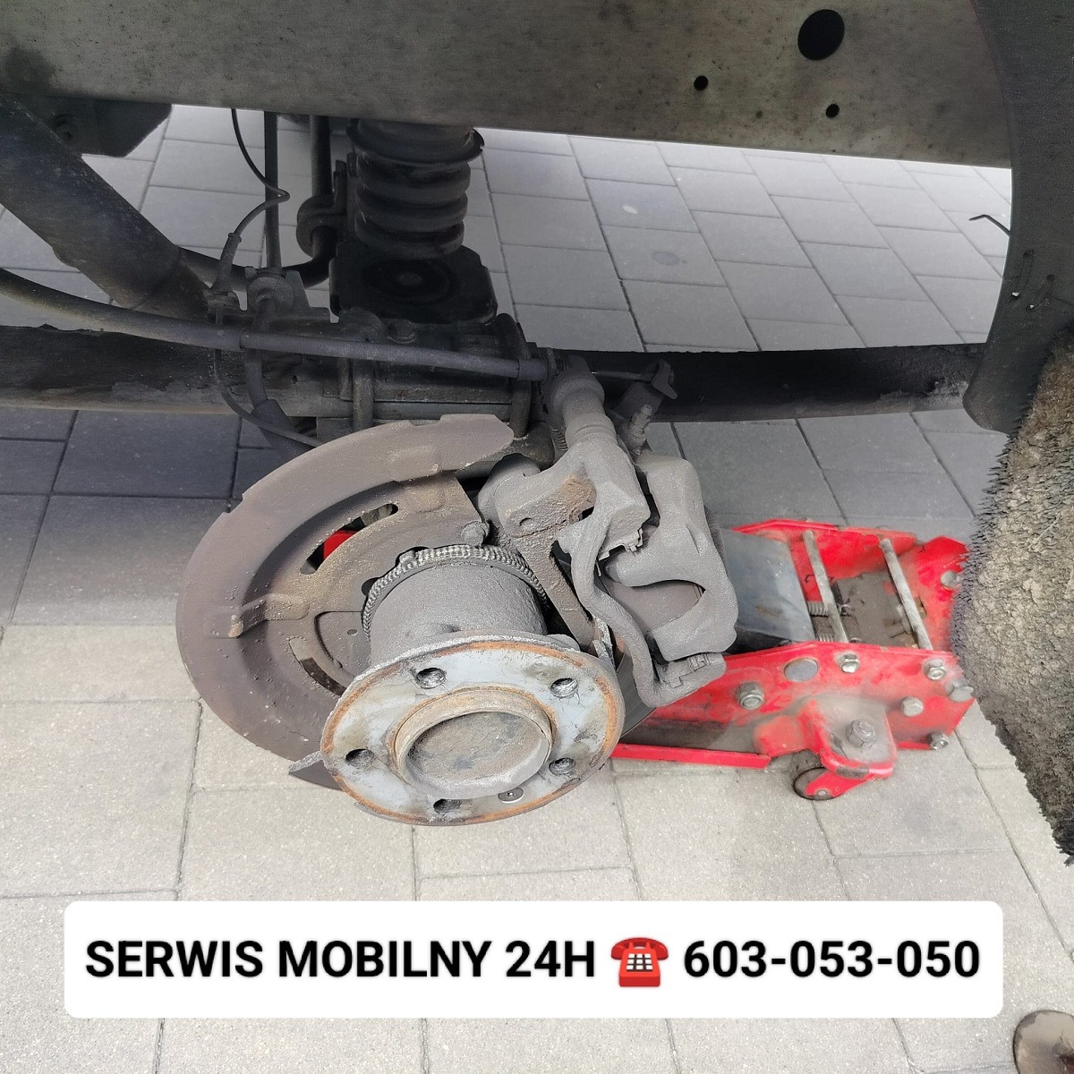 Tylne zawieszenie samochodu na podnośniku hydraulicznym z odsłoniętą tarczą hamulcową i zaciskiem, widok od dołu.