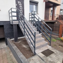 Karo-Met - Zewnętrzne schody z metalową balustradą prowadzące do drzwi wejściowych, wykończone płytkami ceramicznymi, z widocznym fragmentem garażu po lewej stronie.