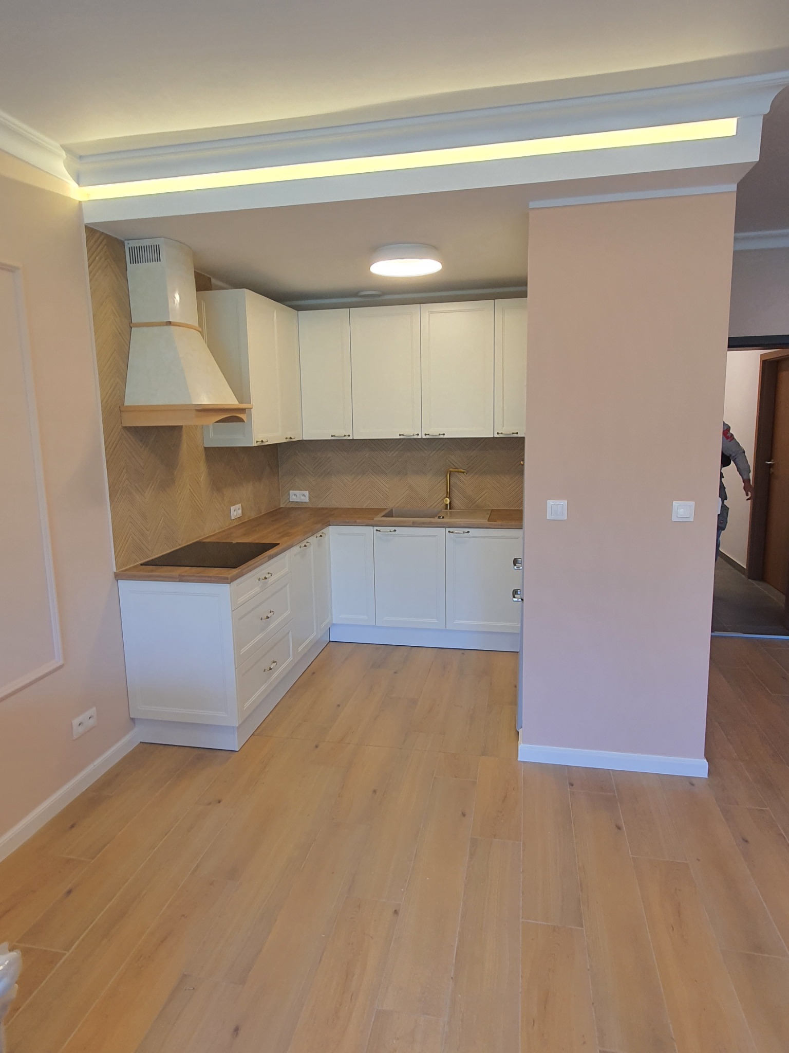 Wykończona kuchnia w Strzelcach Opolskich z białymi szafkami, drewnianymi blatami i podłogą, oraz dekoracyjnym okapem i oświetleniem podszafkowym.