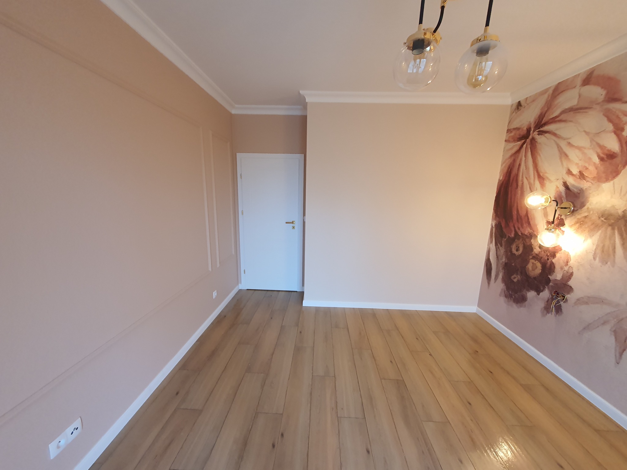 Jasne, przestronne wnętrze po remoncie: parkiet z naturalnego drewna, ściany w odcieniach pudrowego różu z subtelnymi listwami dekoracyjnymi, ozdobna tapeta z motywem kwiatowym i nowoczesne lampy...