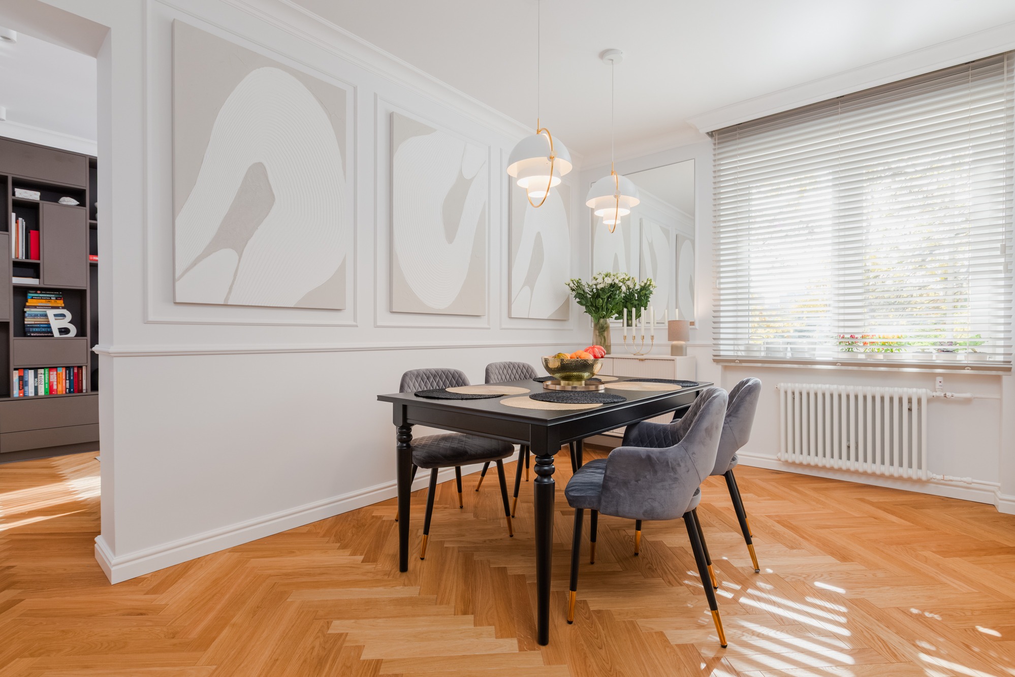 Elegancka jadalnia w Papierni: czarny stół z szarymi krzesłami na parkiecie w jodełkę, minimalistyczne obrazy na ścianie, designerskie lampy i dekoracje.