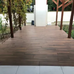 Ułożona podłoga z płytek imitujących drewno na zewnątrz w Tarczynie, widok na ogród i drewnianą konstrukcję z pnączami.