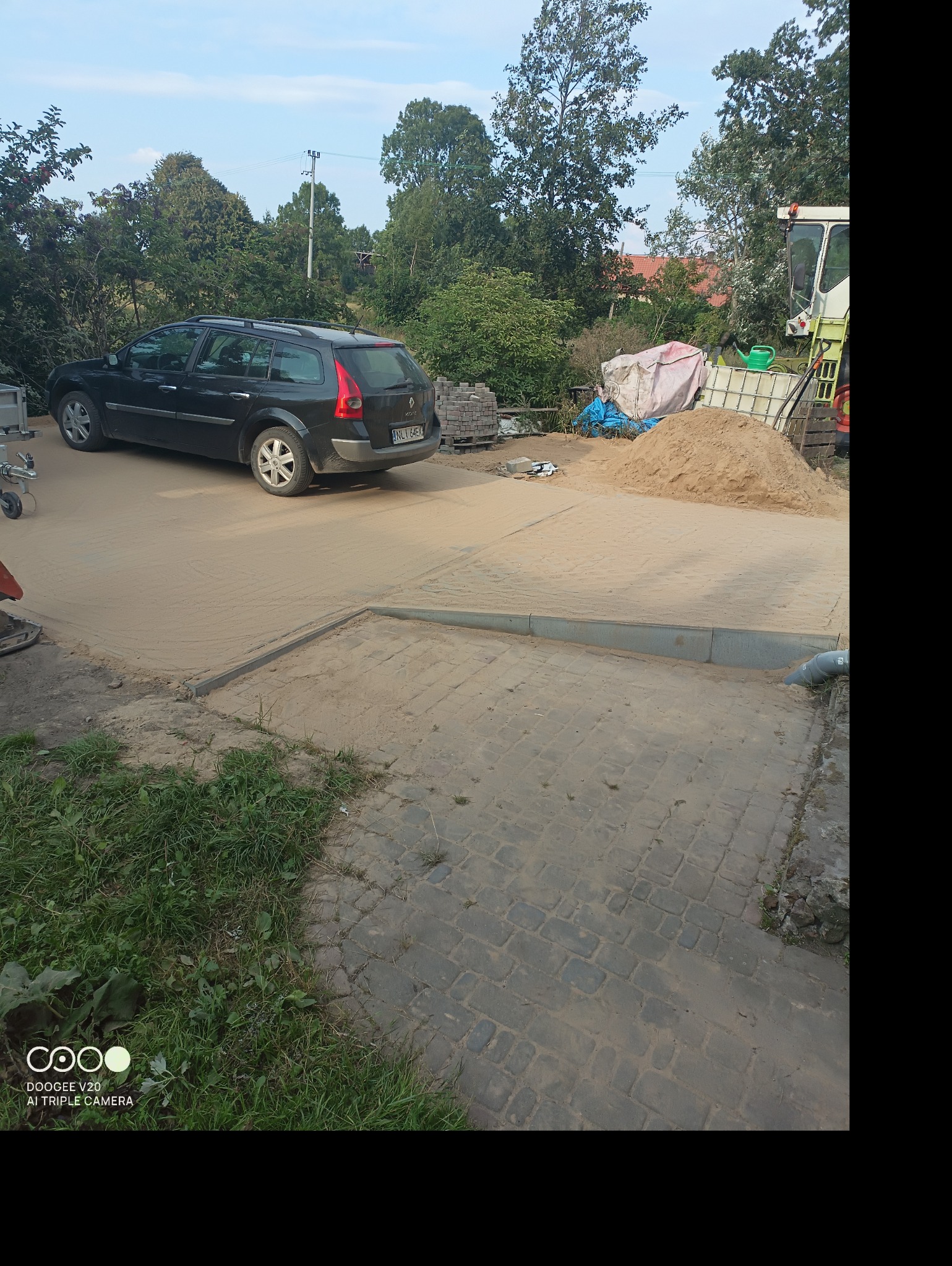 Układanie kostki brukowej na podbudowie z piasku, widoczny fragment ułożonej kostki, krawężnik i zaparkowany samochód osobowy.