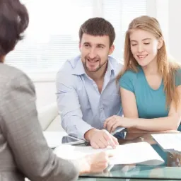 Para analizuje dokumenty z doradcą finansowym przy szklanym stole, w tle jasne wnętrze biura.