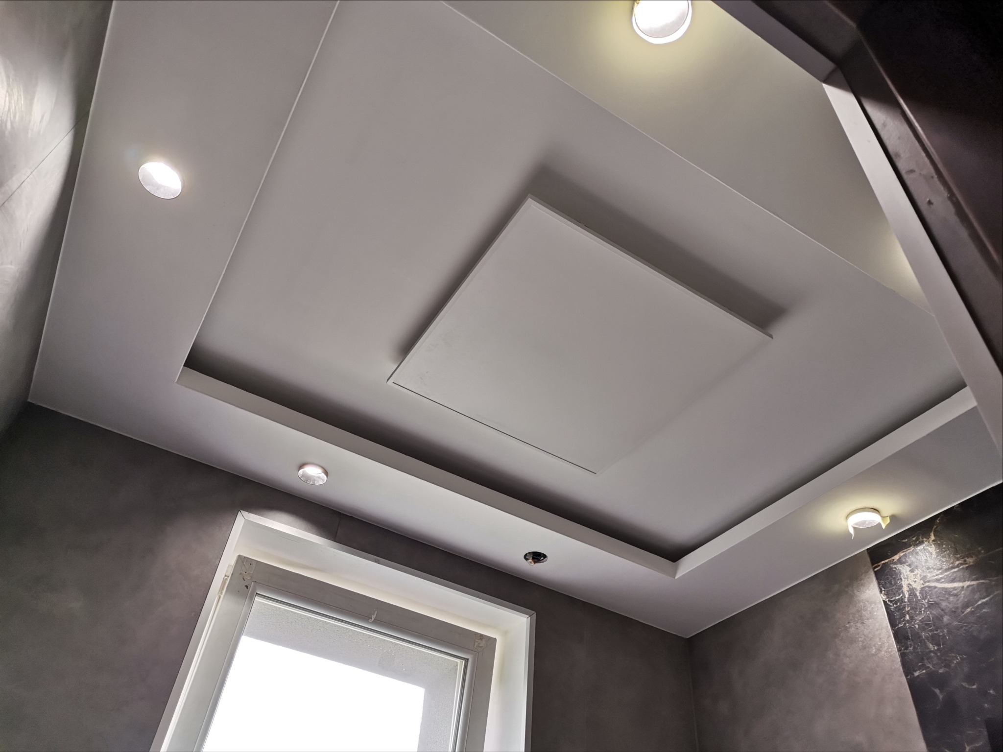 Nowoczesny sufit podwieszany z oświetleniem punktowym LED w łazience z szarymi ścianami i oknem.