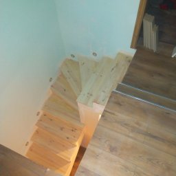 Ihrhause - Widok z góry na drewniane schody w trakcie montażu, z widocznymi punktowymi lampkami w ścianie i fragmentem drewnianej podłogi.