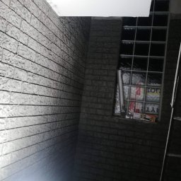 Ihrhause - Wnętrze z dekoracyjną ścianą imitującą cegłę, okno z luksferami i fragment drabiny malarskiej.