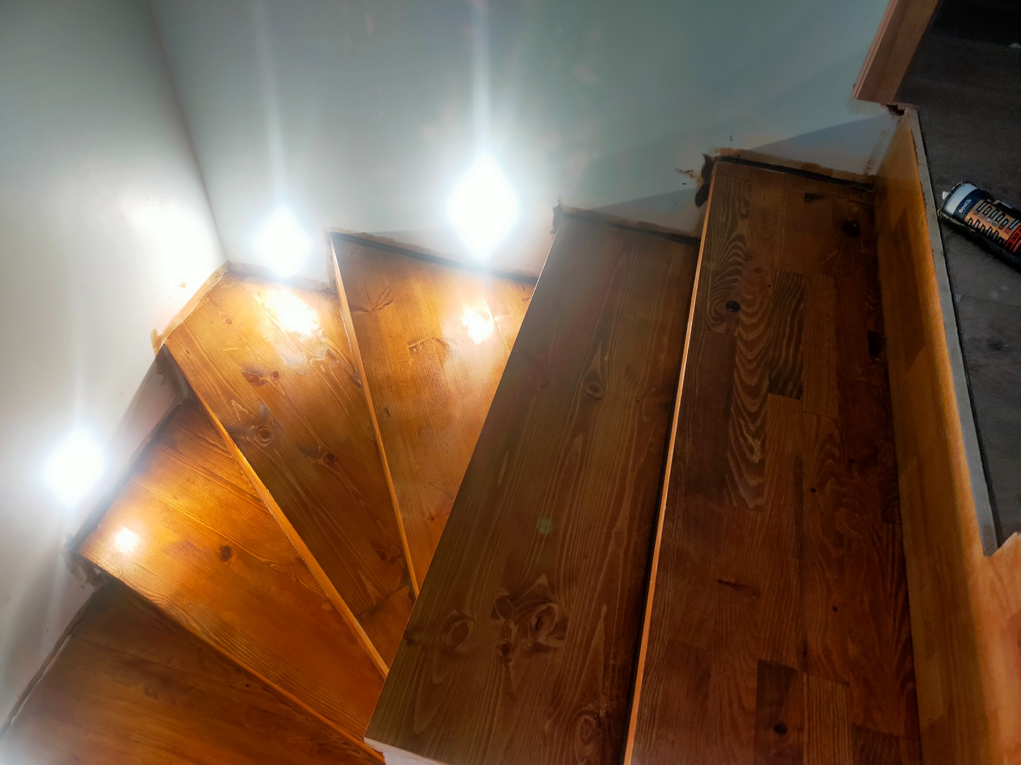 Drewniane schody spiralne podczas montażu, widoczna puszka z uszczelniaczem przy krawędzi, surowy stan wykończenia ścian.