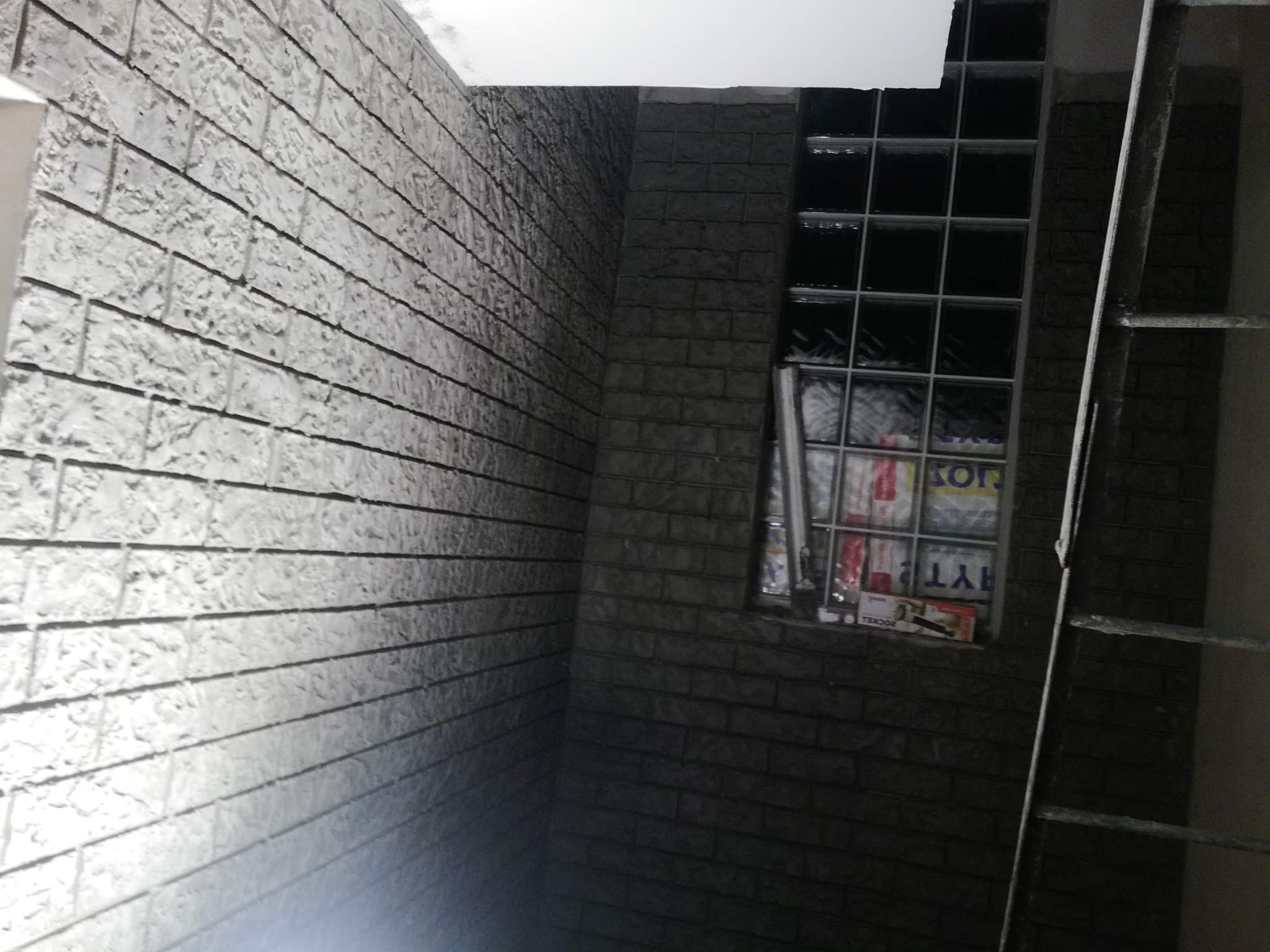 Wnętrze z dekoracyjną ścianą imitującą cegłę, okno z luksferami i fragment drabiny malarskiej.