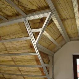 Szkielet z metalowych profili pod zabudowę poddasza, widoczna warstwa izolacji z wełny mineralnej, drewniane elementy konstrukcyjne dachu w tle.