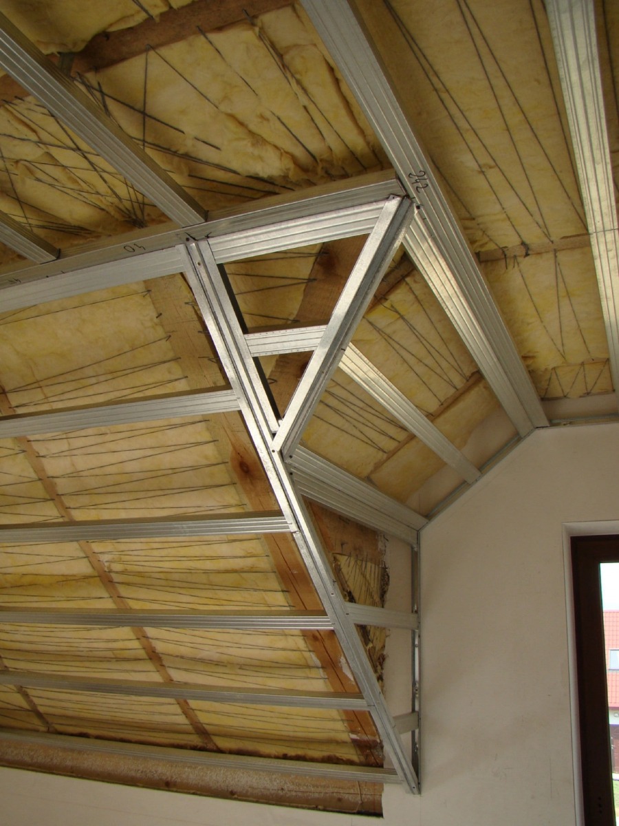 Szkielet z metalowych profili pod zabudowę poddasza, widoczna warstwa izolacji z wełny mineralnej, drewniane elementy konstrukcyjne dachu w tle.