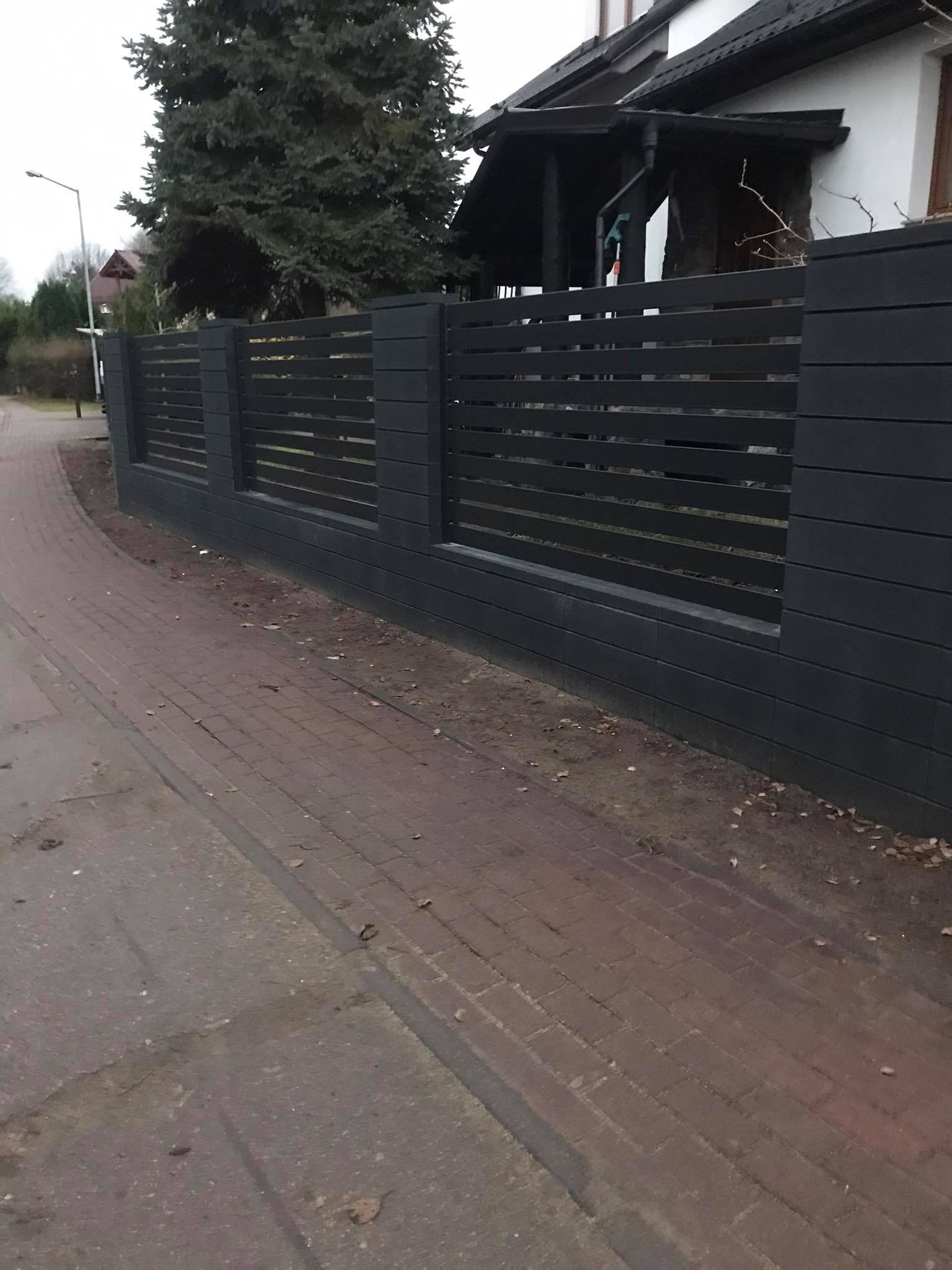 Nowoczesne, ciemnoszare ogrodzenie panelowe z poziomych desek, przylegające do chodnika z czerwonej kostki brukowej, z domem w tle.