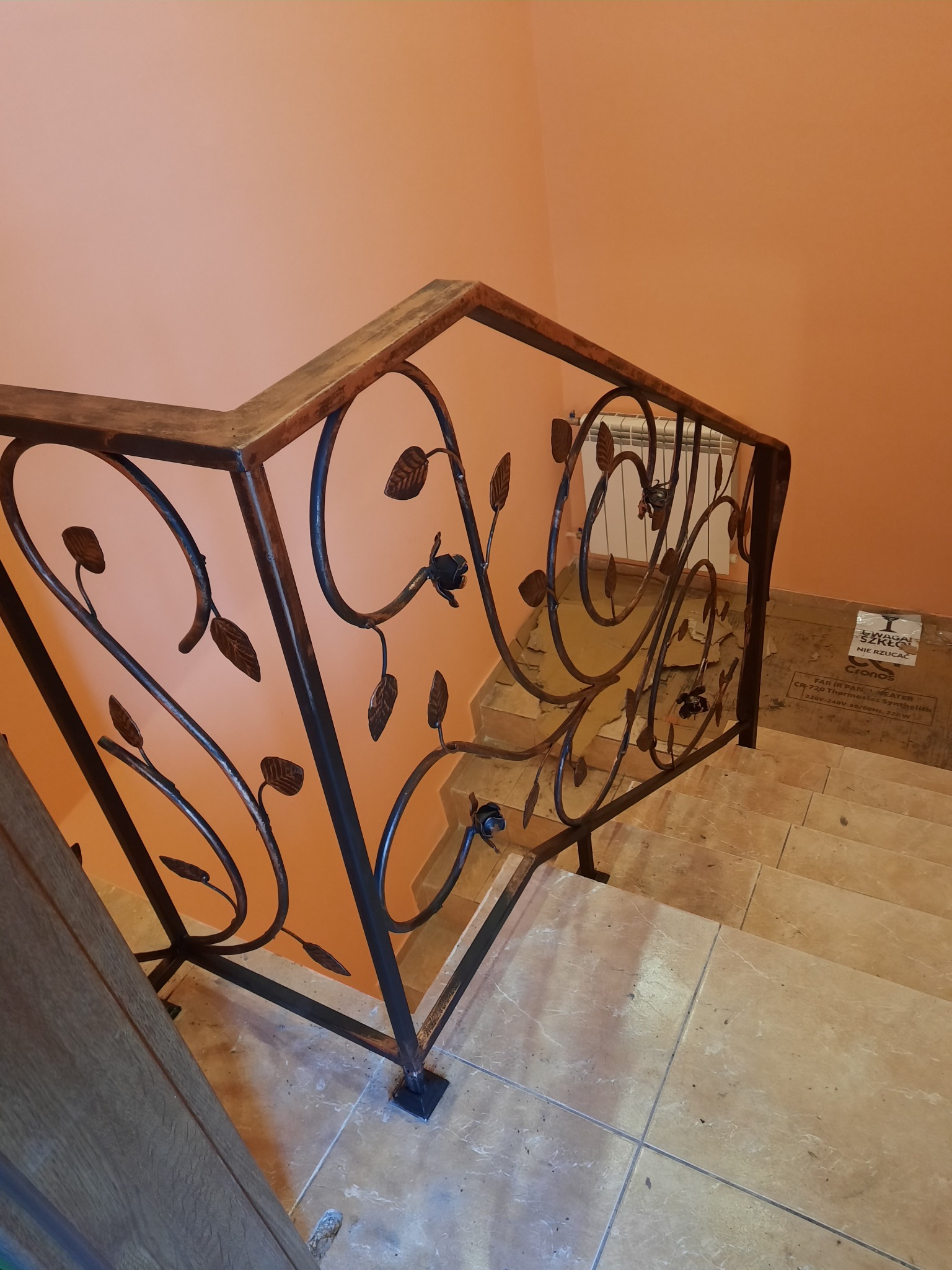 Kuta balustrada schodowa z motywem roślinnym, widok z góry na schody wyłożone płytkami, pomarańczowa ściana w tle.