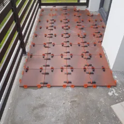 Układanie brązowych płytek na balkonie z użyciem poziomujących klipsów i klinów, widoczna balustrada i fragment ściany budynku.