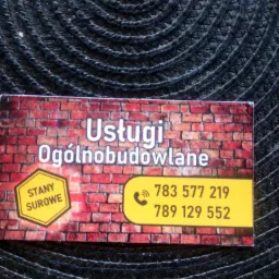 Wizytówka firmy budowlanej z napisem 'Usługi Ogólnobudowlane' i numerami telefonów, tło imitujące mur z cegły, leży na ciemnej plecionej podkładce.