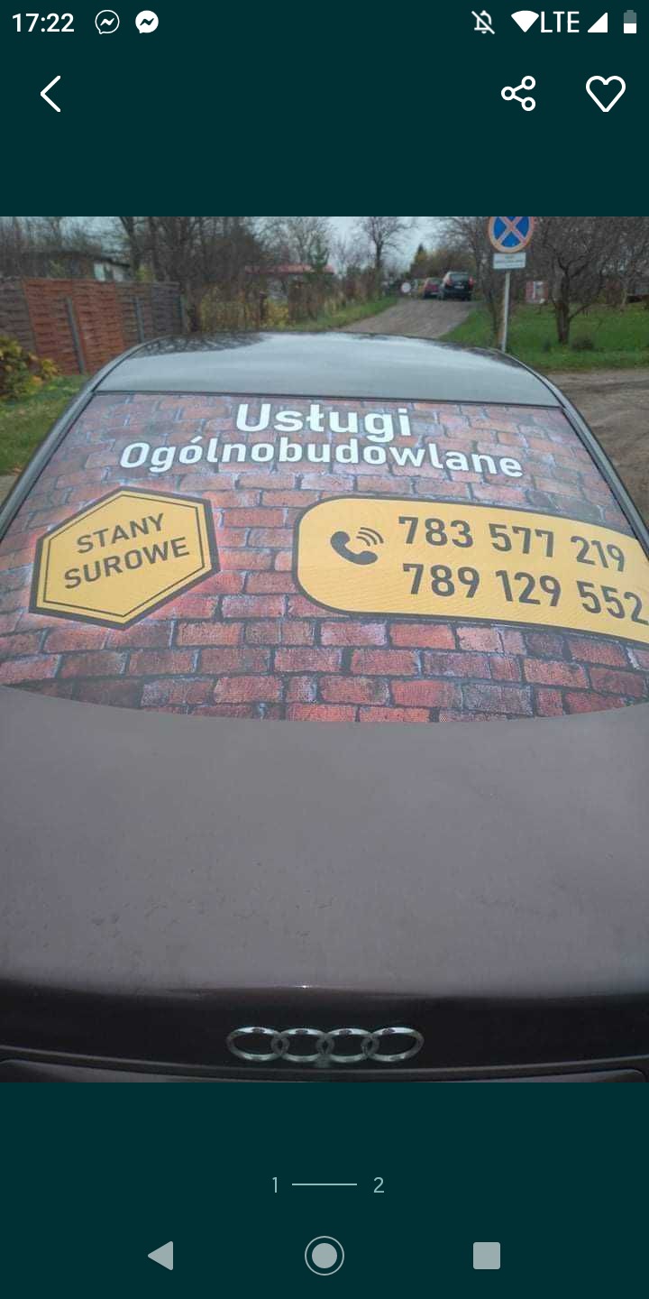 Tylna szyba samochodu z reklamą usług ogólnobudowlanych, stanów surowych oraz numerami telefonów na tle imitacji muru z cegły.