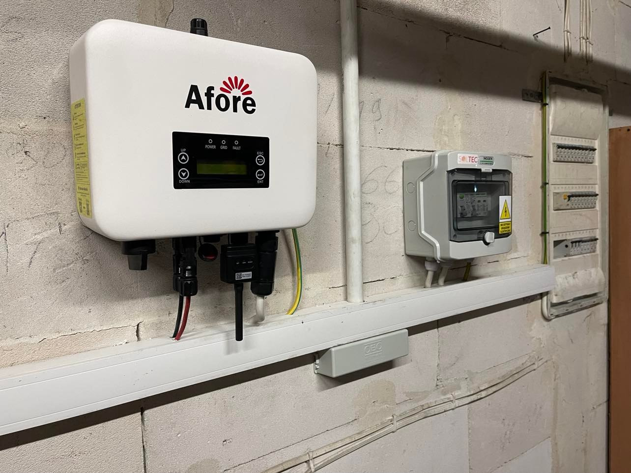 Biały falownik Afore zamontowany na ścianie z betonu komórkowego obok szarej skrzynki elektrycznej Soltec i rozdzielnicy elektrycznej.