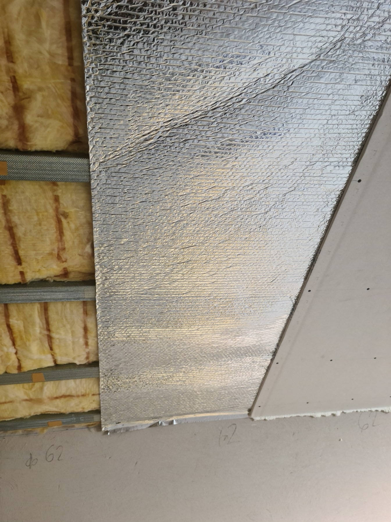 Montaż izolacji z folią aluminiową i płyty gipsowo-kartonowej na suficie, widoczne profile metalowe i wełna mineralna.