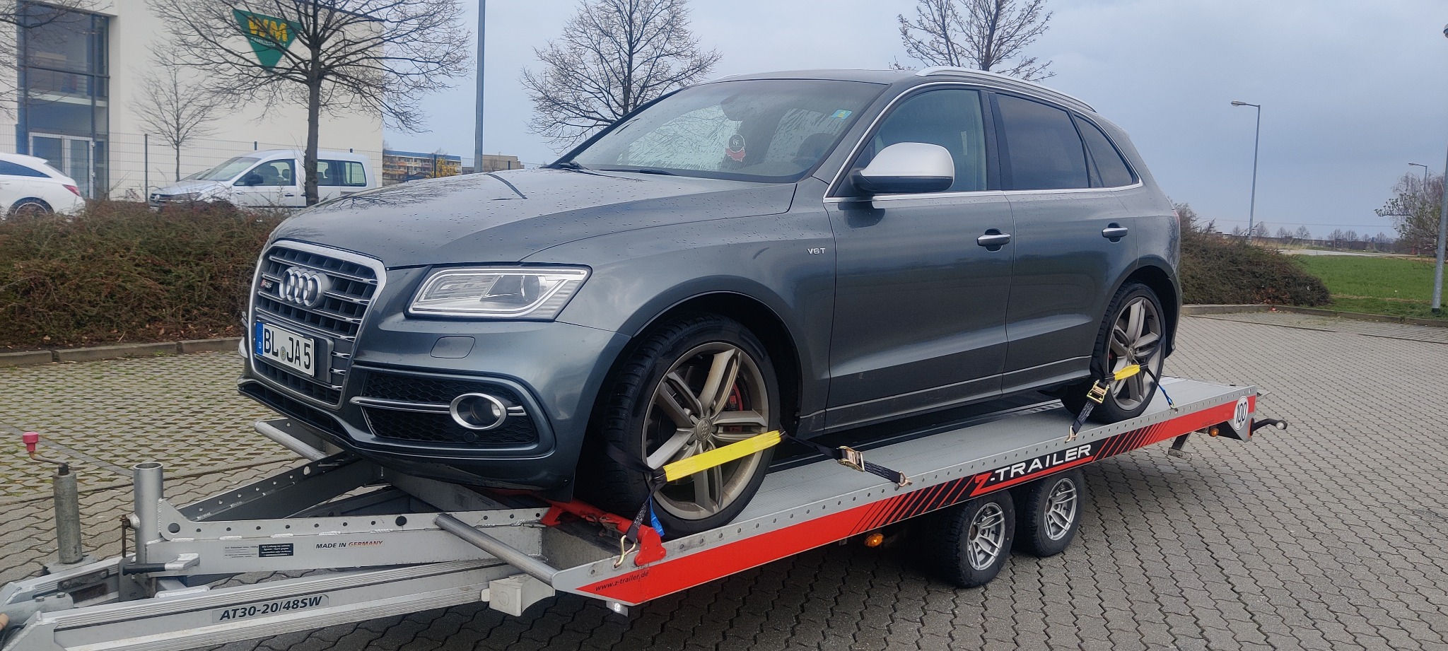 Szary samochód Audi Q5 V6T zabezpieczony pasami na platformie lawety z widoczną tablicą rejestracyjną BL JA 5, stojącej na kostce brukowej.