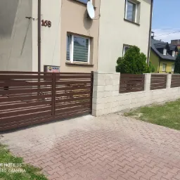 Automatyczna brama przesuwna z poziomymi profilami w kolorze brązowym, zamontowana przy posesji z numerem 168, widoczna kostka brukowa i fragment trawnika.