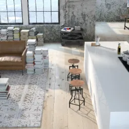 Jasne, przestronne wnętrze loftu z nowoczesną białą kuchnią, drewnianymi stołkami barowymi i widokiem na salon z brązową sofą otoczoną stertami książek.