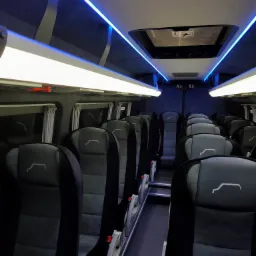 Wnętrze autobusu w Czeladzi z czarnymi skórzanymi fotelami z białym logo, oświetlenie LED w kolorze białym i niebieskim.