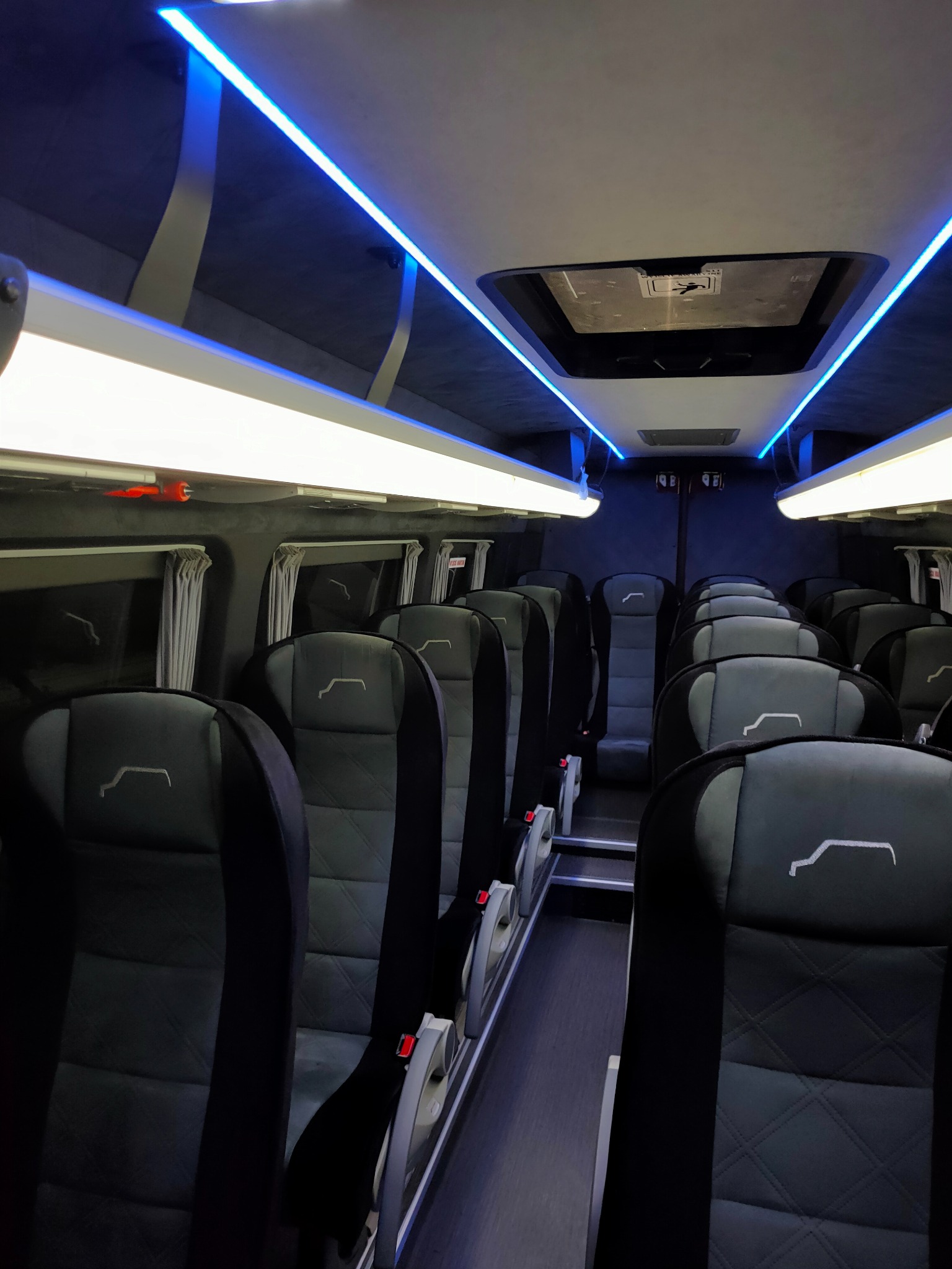 Wnętrze autobusu w Czeladzi z czarnymi skórzanymi fotelami z białym logo, oświetlenie LED w kolorze białym i niebieskim.
