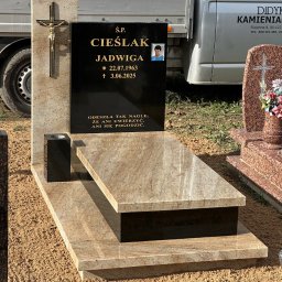 Kamieniarstwo Robert Didyk - Jasny, dwupoziomowy nagrobek z piaskowca z czarną tablicą i złotym krzyżem, na tle częściowo widocznego samochodu dostawczego i innych nagrobków na cmentarzu.