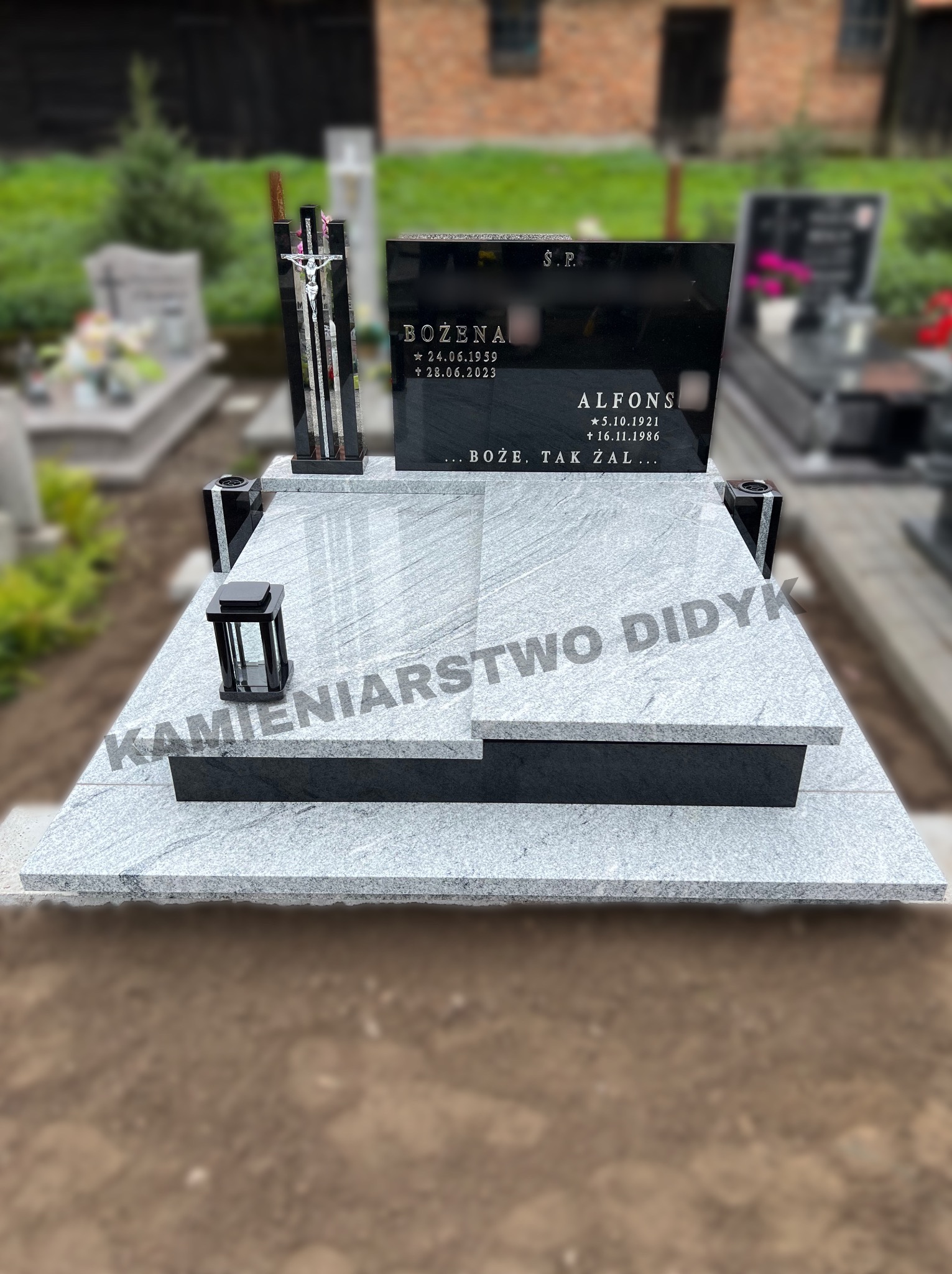 Granitowy pomnik z czarną tablicą nagrobną z wygrawerowanymi imionami i datami, uzupełniony o czarny lampion i krzyż, na tle innych nagrobków.