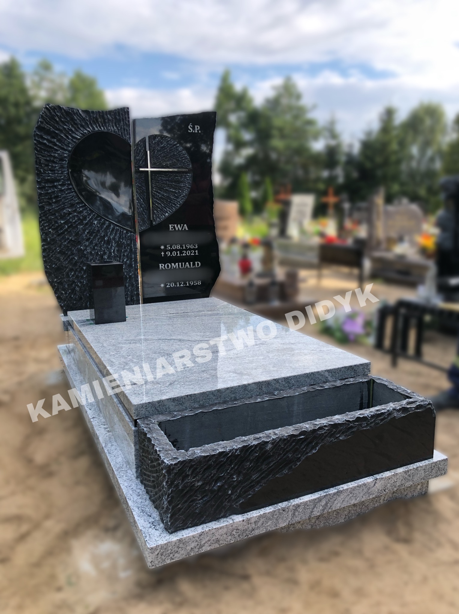 Nowoczesny, dwukolorowy pomnik z ciemnego granitu z motywem serca i krzyża, jasnoszary cokół, na tle cmentarza.