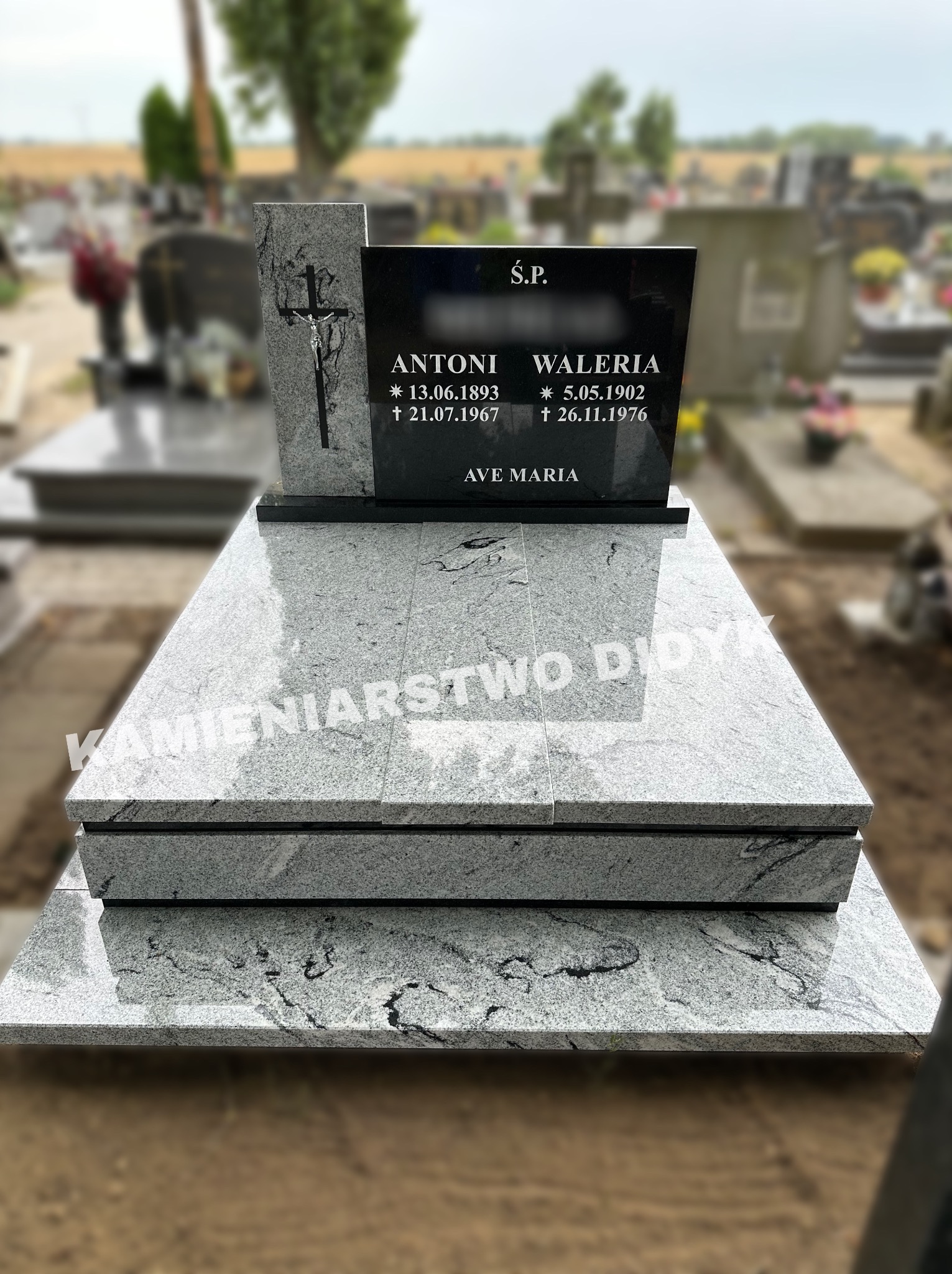 Granitowy pomnik nagrobny z czarną tablicą inskrypcyjną i krzyżem, z napisem 'Ś.P. Antoni Waleria' oraz datami urodzin i śmierci, umieszczony na cmentarzu.