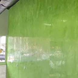 Ściana w biurze pomalowana na jaskrawy zielony kolor z efektem dekoracyjnym, widoczne gniazdka elektryczne i elementy wentylacji pod sufitem.