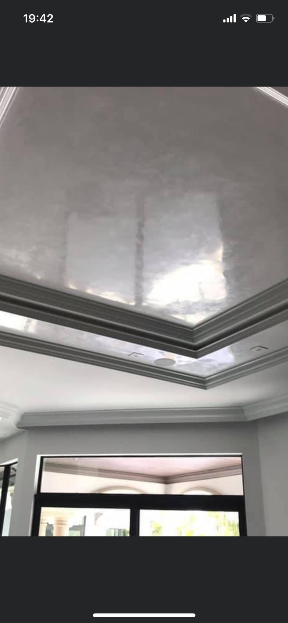 Błyszcząca, srebrzysta gładź na suficie z dekoracyjnymi listwami przysufitowymi, widok z dołu na fragment okna.