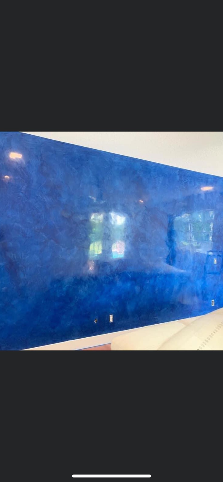 Ściana w pokoju pomalowana na niebiesko z efektem ombre i delikatną strukturą, widoczne gniazdka elektryczne i fragment białej listwy przypodłogowej oraz narożnik jasnej sofy.