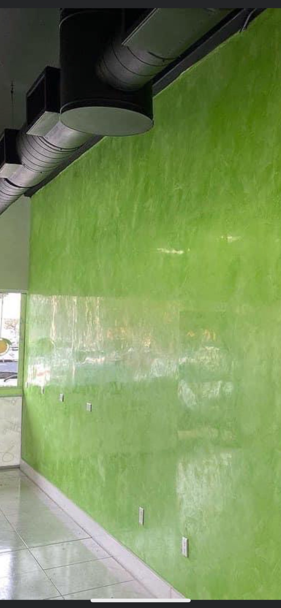 Ściana w biurze pomalowana na jaskrawy zielony kolor z efektem dekoracyjnym, widoczne gniazdka elektryczne i elementy wentylacji pod sufitem.