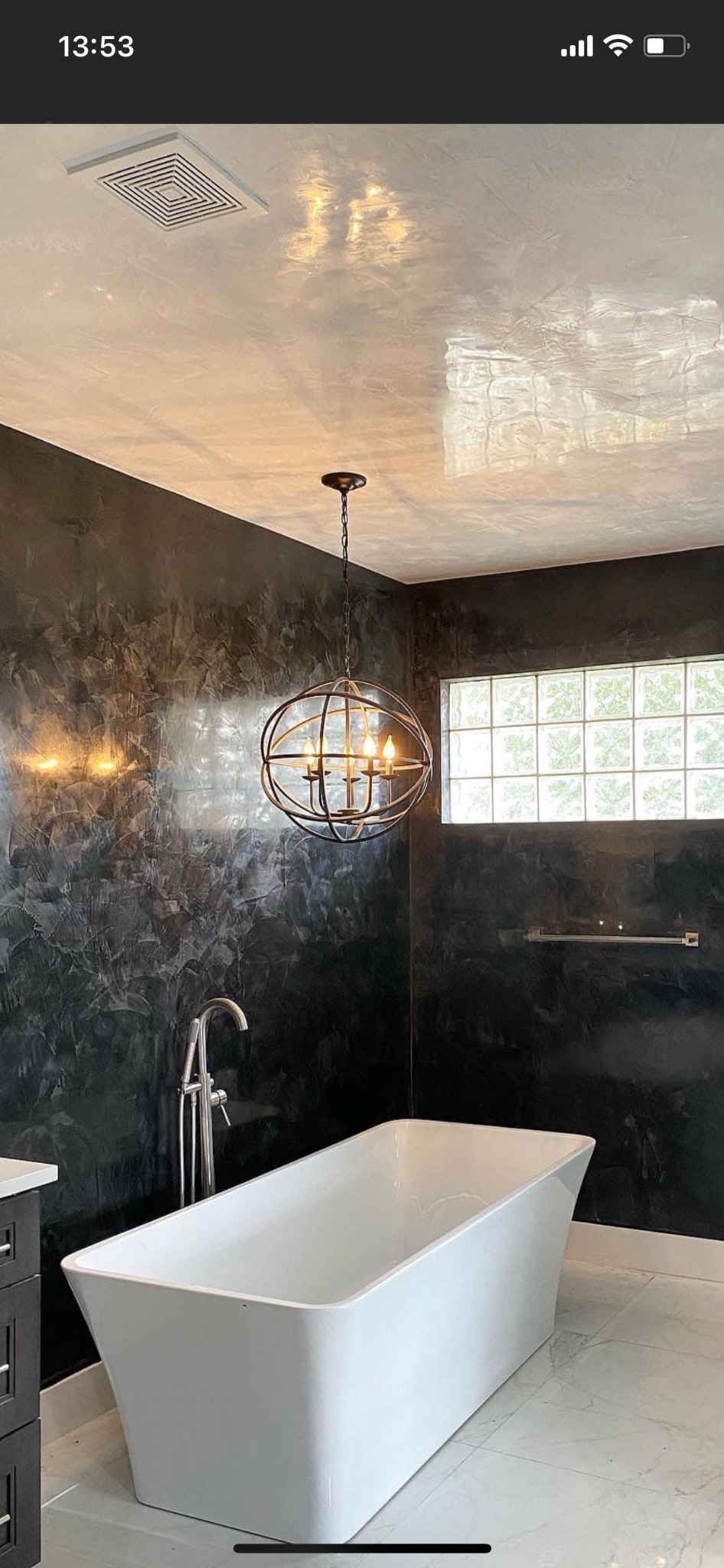 Nowoczesna łazienka z czarnymi ścianami wykończonymi efektem dekoracyjnym, białą wanną wolnostojącą, okrągłą lampą wiszącą i marmurową podłogą.