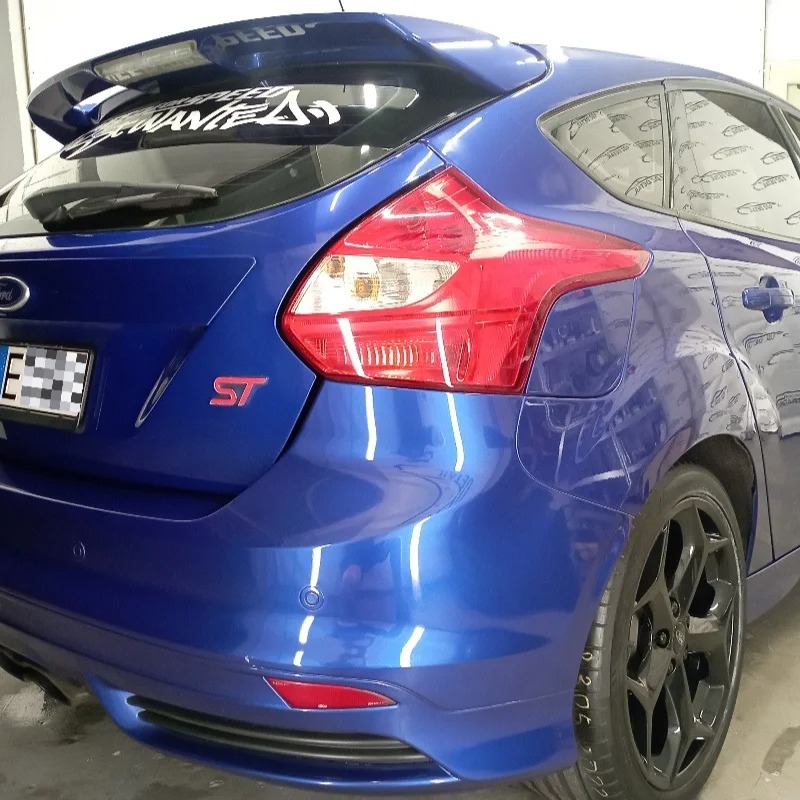 Błyszczący, niebieski Ford Focus ST po umyciu, widoczny z tyłu, z naklejkami na spojlerze i czarnymi felgami.